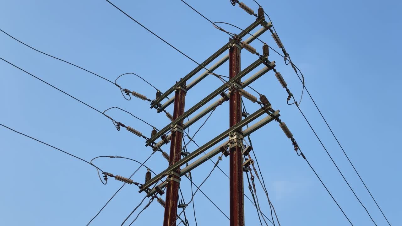Static shot of a power transmission tower against a clear blue sky. The tower is constructed from metal and features multiple wires and insulators