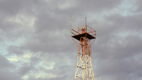 rotating beacon light, mounted on a tower at a small airport, is shown in the evening, set against a strong clouds