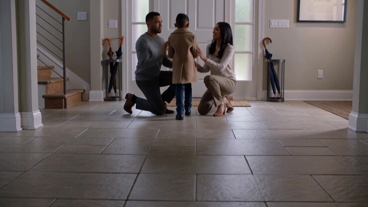 Smoothing child's beige coat, smart parents kneeling guiding child opening foyer door to go outside