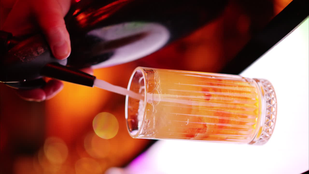 Un barman versa la soda in un bicchiere con ghiaccio al bar di notte con luci al neon rosse, rallentatore, schermo verticale
