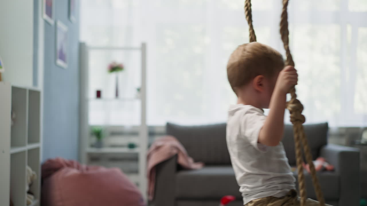 Calm toddler boy rides on swing in light living room
