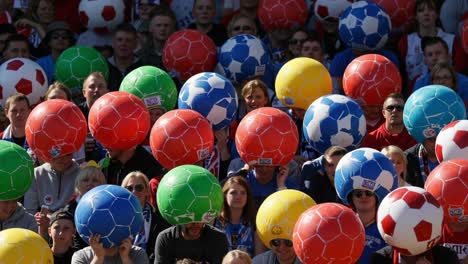a vibrant crowd displays colorful soccer balls in unison at an outdoor event, creating a festive atmosphere of sports enthusiasm and community spirit
