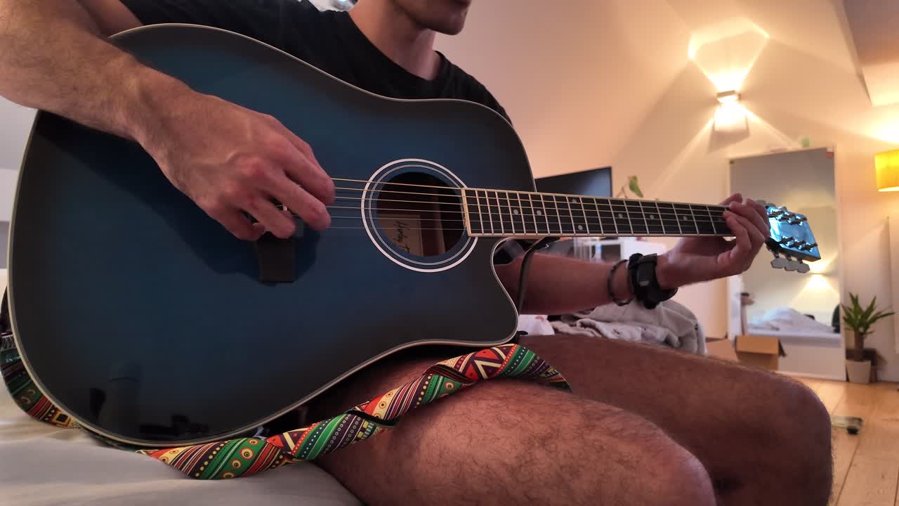 Man playing acoustic guitar while sitting on bed indoors
