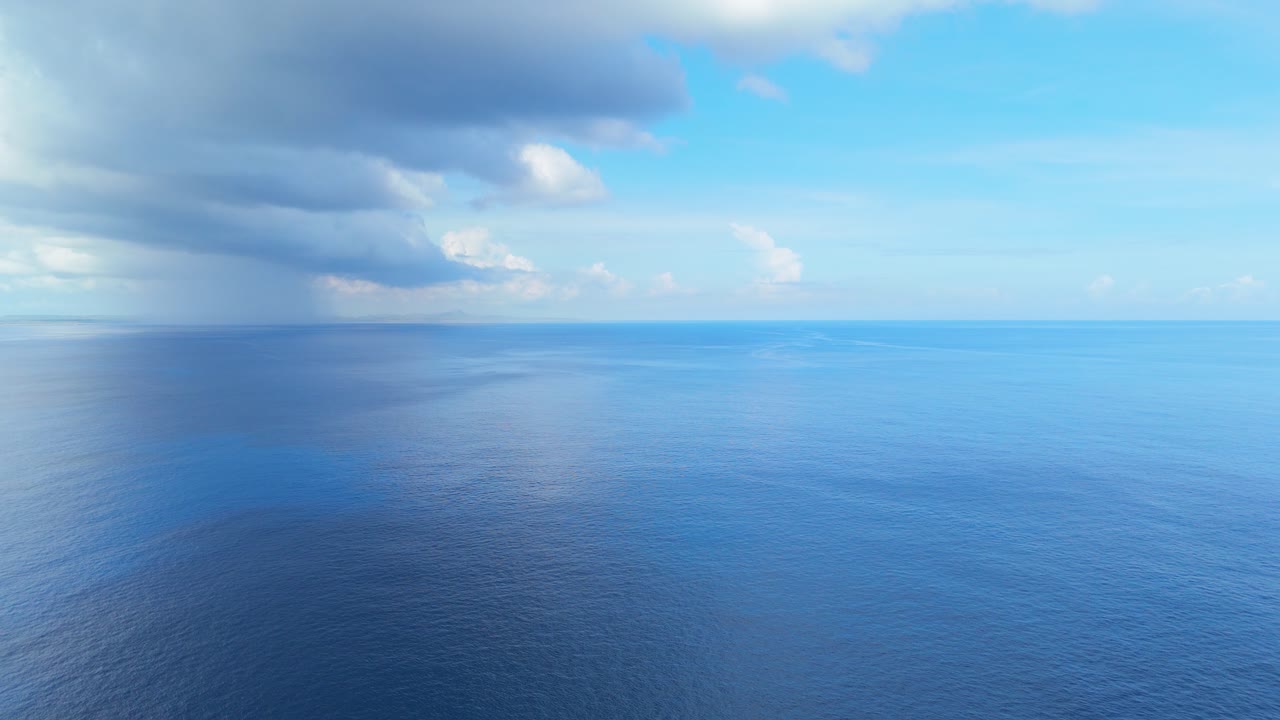 Vista aerea da drone di un oceano calmo con superficie a specchio e la costa distante di Curaçao sotto nuvole temporalesche.