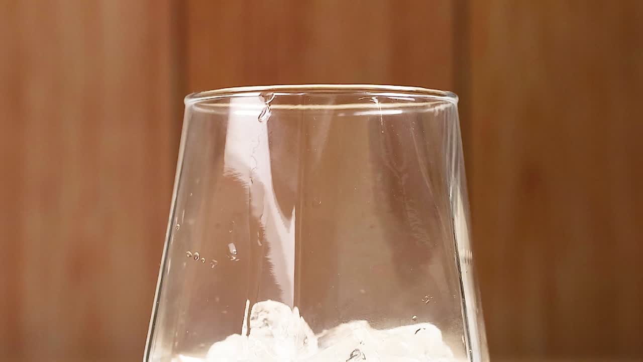Close-up in slow motion van bevroren ijsblokjes die in een leeg transparant drinkglas vallen