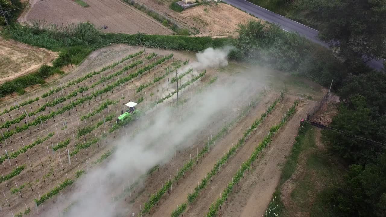 Ripresa aerea di un trattore compatto nascosto nella polvere mentre ara il terreno tra i vigneti esistenti