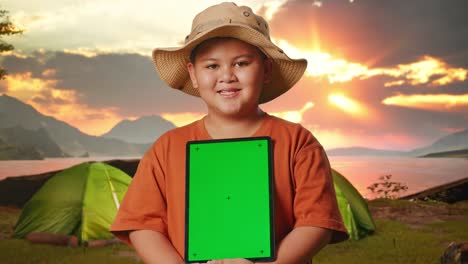 smiling boy holding green screen tablet at sunset campground