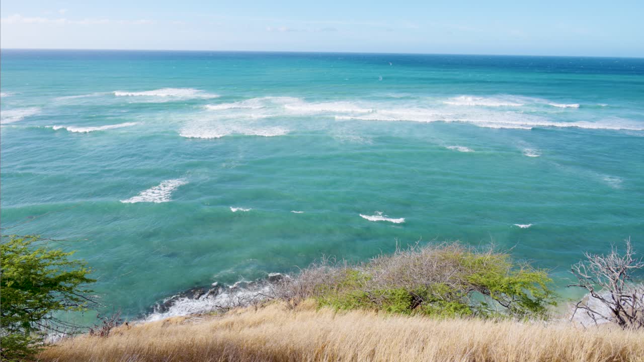 Vista mozzafiato dall'alto da una scogliera che si affaccia sull'oceano Pacifico turchese, con onde delicate che si infrangono sulla riva rocciosa in una bella giornata di sole a Honolulu, Hawaii.
