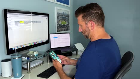 Home-Working-Bearded-Caucasian-Male-Sitting-At-Computer-Grabbing-cell-phone-checking-Messages