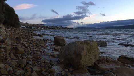 Slow-motion-waves-rolling-in-past-rocks-with-blue-and-orange-dusk-sun-setting-in-sky