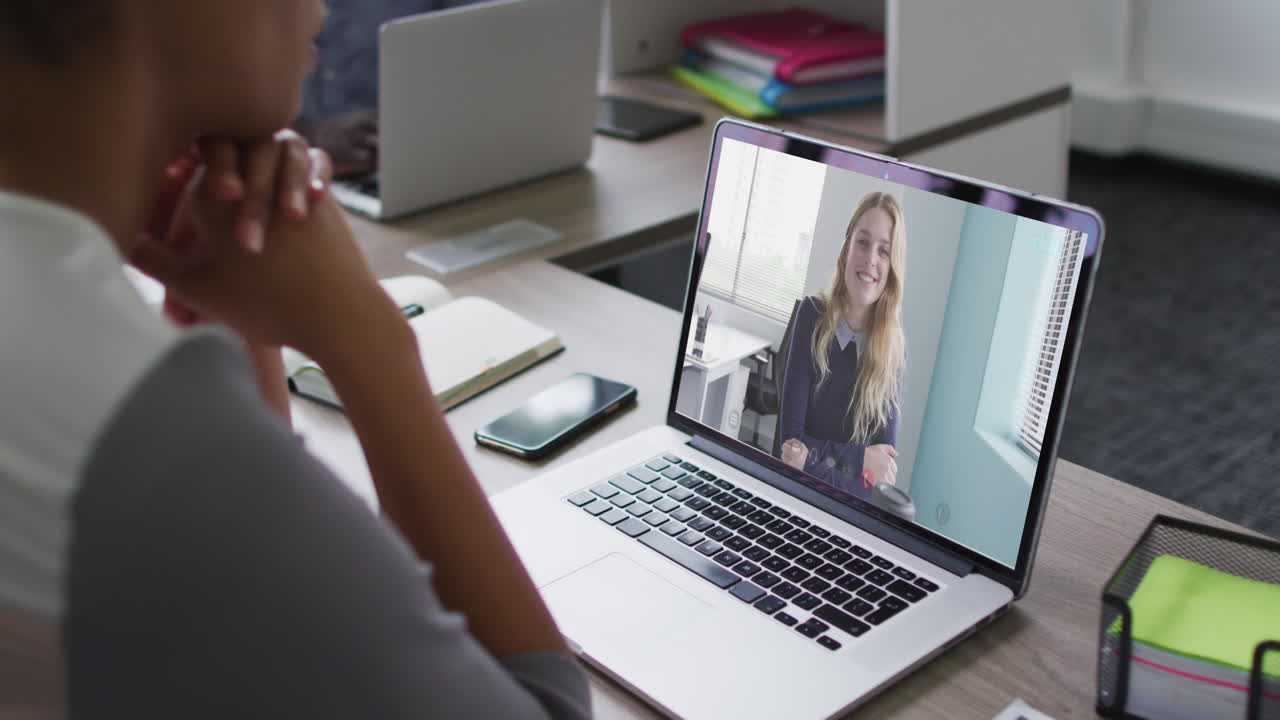 African american businesswoman sitting at desk using laptop having video call with female colleague