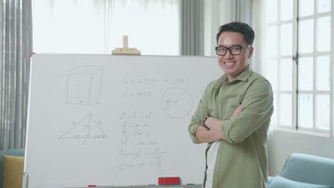asian male teacher with glasses crossing arms and smiling to camera while teaching math at home