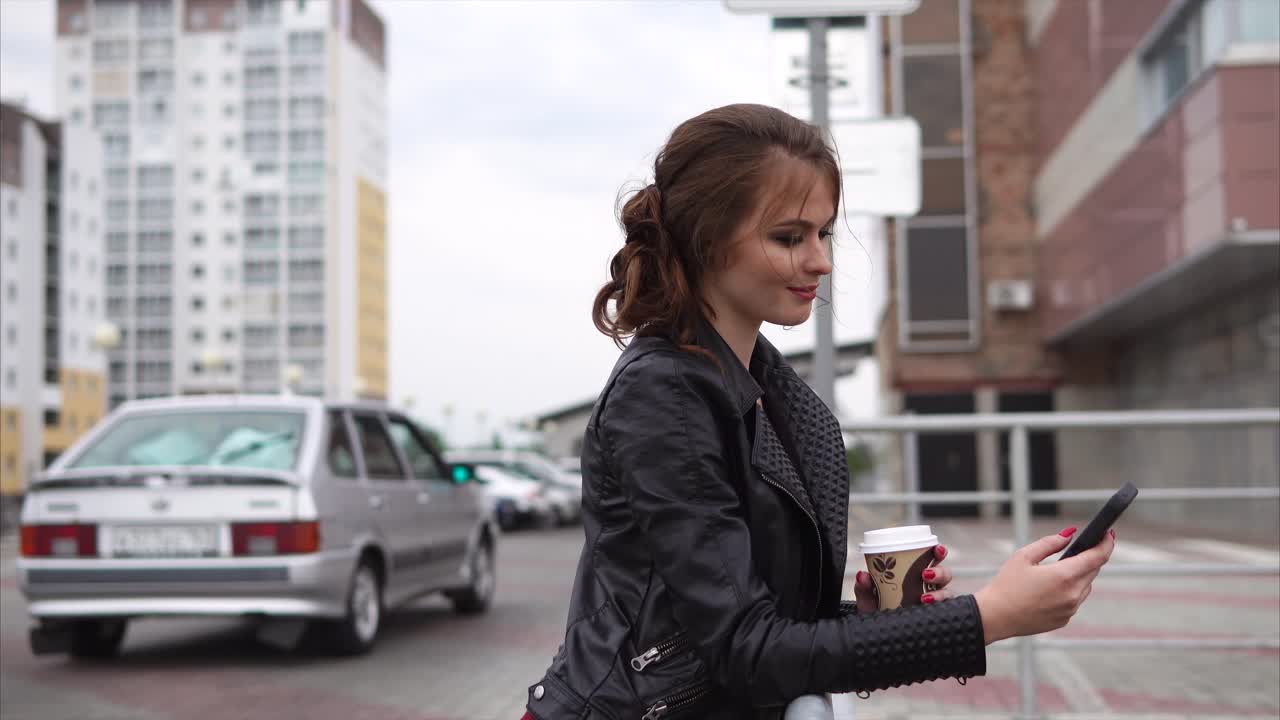 Young woman using a smartphone while drinking coffee outdoors in a city