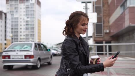 young woman using a smartphone while drinking coffee outdoors in a city