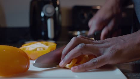 hands of a man dicing yellow bell pepper slices with a big knife