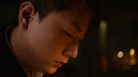 sad asian man alone, head slightly bowed, focused on something in front of him