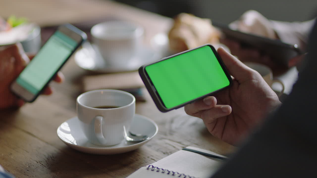 close up business people hands using smartphone greenscreen browsing working online collaborating on mobile phone chroma key networking together friends drinking coffee in cafe enjoying lifestyle