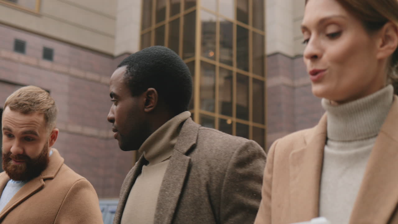 Two caucasian and african businessman and caucasian businesswoman talking about their work while walking on the street