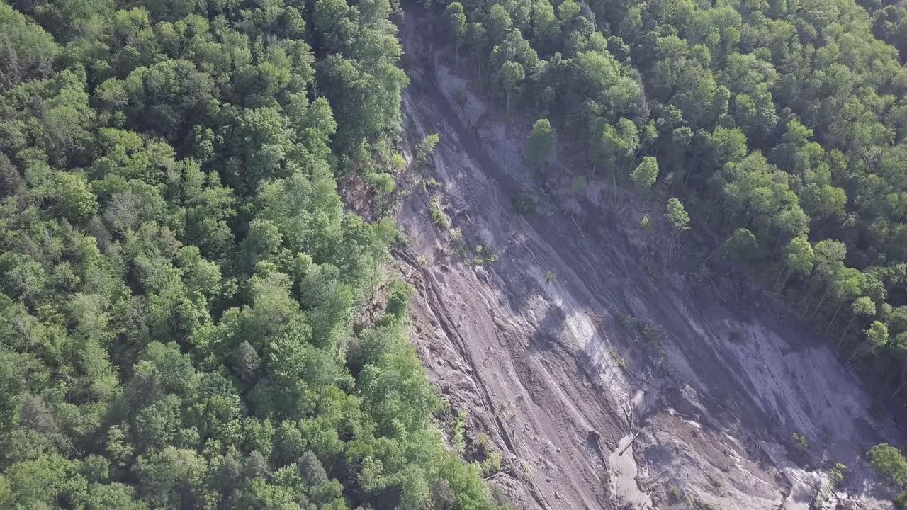 Smooth rotating aerial drone shot of a large, 20+ acre landslide on a steep forest slope, with downed trees and mud visible to the river