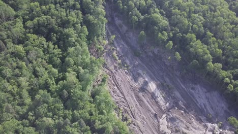 smooth rotating aerial drone shot of a large, 20+ acre landslide on a steep forest slope, with downed trees and mud visible to the river