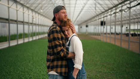 a loving couple a girl with red hair and her boyfriend in a farmers cap stand among young plants and sprouts in a greenhouse on a farm