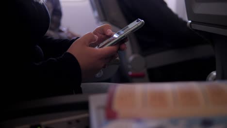 close-up of a woman passenger on an airplane holding a phone during the flight.