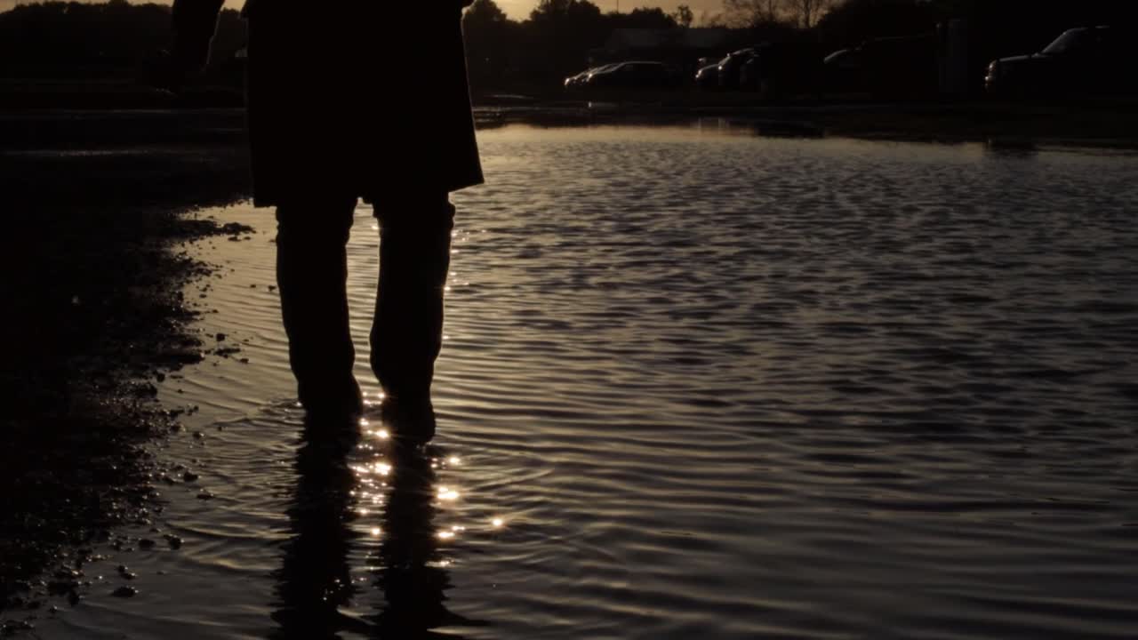 Silhouette di persona che cammina tra le increspature dell'acqua al tramonto