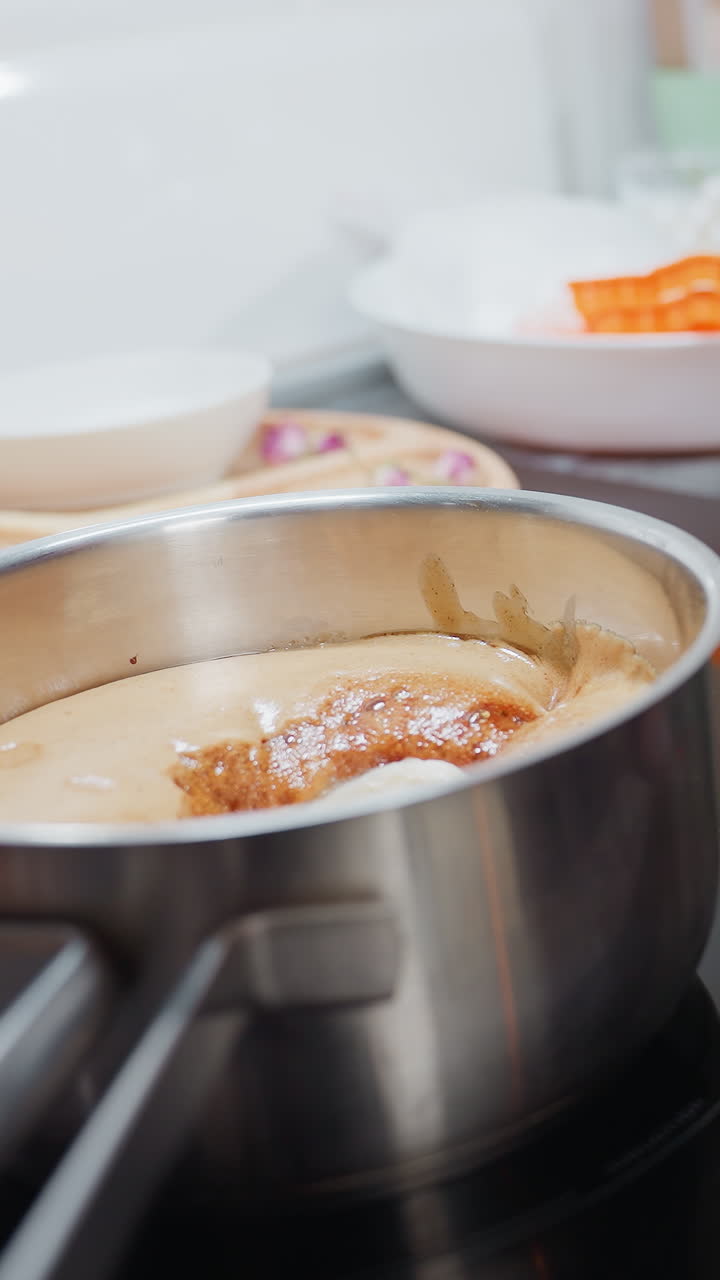 Close-up of food cooking on electric stove with various kitchen utensils nearby as person wipes sleek glass surface with cloth in clean, modern kitchen, smooth countertop and organized workspace