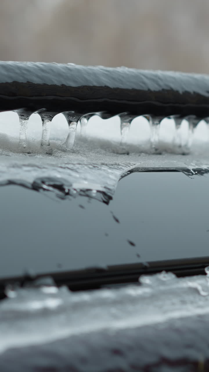 두꺼운 얼음과 눈으로 인 차량 지붕의 클로즈업, 검은 금속 레일의 가장자리를 따라 형성되는 아이스클을 강조하고, 흐릿한 도시 겨울 배경에 맞춰 설정