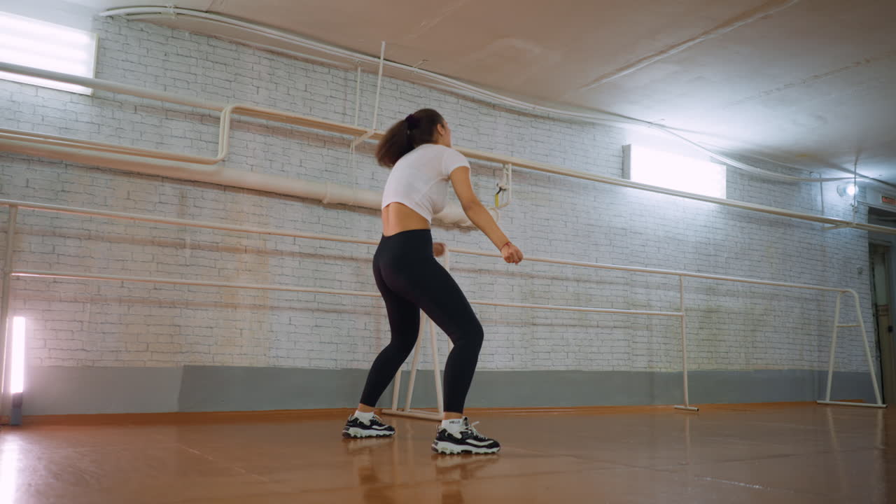 Young lady in casual wear twisting body dancing and jumping with energetic motion, joyful expressive movement, lively body language, indoor casual setting, dynamic female performer