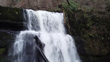 A-drone-shot-of-a-waterfall,-starting-wide-and-pushing-closer,-up-and-over-the-top-of-the-falls