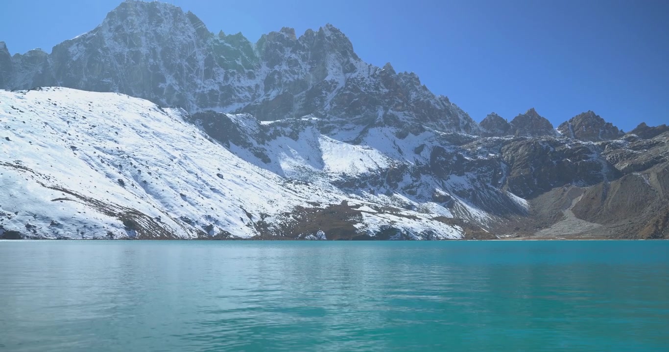 Gokyo Gölleri, Everest Nepal: El değmemiş turkuaz göl suyundan Ngozumpa Buzulu'nu ve berrak mavi gökyüzü altında yükselen, karla kaplı Himalaya dağ zirvelerini ortaya çıkarmak için kamera yukarı doğru eğiliyor.