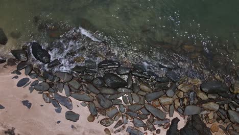 drone vertical tracking shot of rocky coastline and beach with small waves