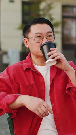 happy asian man enjoying drinking morning coffee hot drink relaxing taking a break on city street