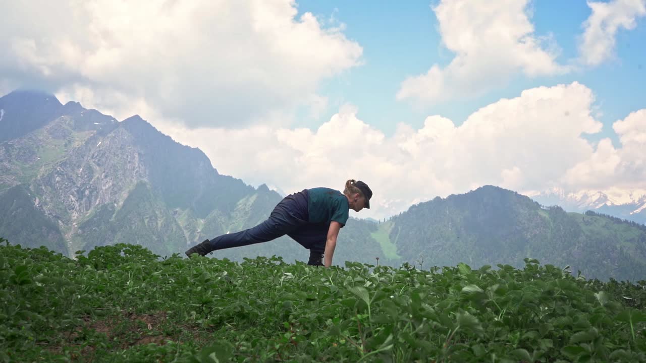 mujer practicando yoga en lamadugh trek haciendo una curva hacia adelante, una estocada baja, un medio círculo y una pose de perro hacia abajo con montañas himalayas y cielo en el fondo en manali, india