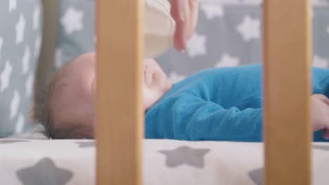 mommy feeds little baby in azure suit with fresh milk in cot