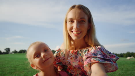 madre e hija posando para la cámara del teléfono móvil en el parque de la ciudad al atardecer
