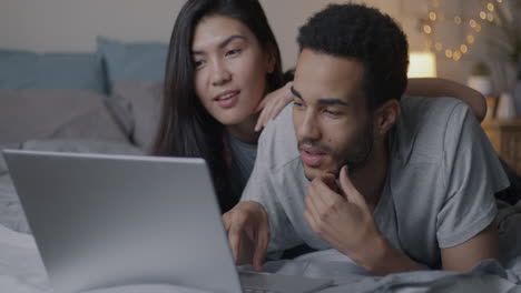 una pareja viendo una computadora portátil en la cama.