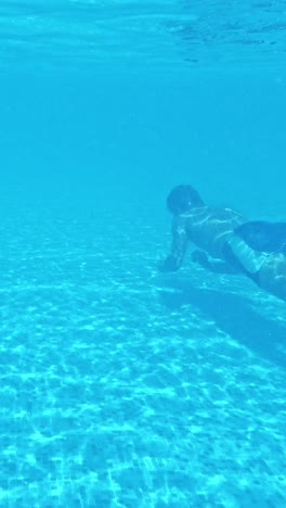 un joven nada bajo el agua en una piscina.