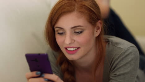 hermosa morena sonriente acostada en el sofá usando un teléfono inteligente