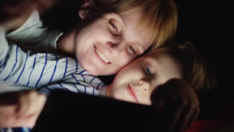 Mother-And-Daughter-Enjoy-The-Tablet-Lie-In-Bed-At-Night