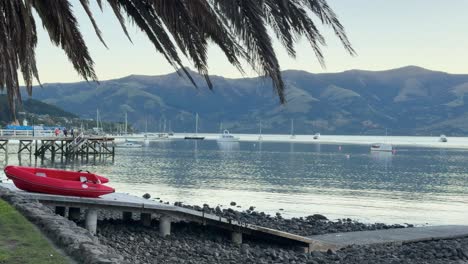 A tranquil lakeside scene with a red kayak, calm waters, and distant hills under soft lighting