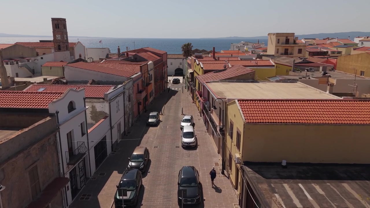 Strada che passa tra gli edifici che costeggiano la via nella città costiera di Portoscuso, nel sud della Sardegna, Italia. Ripresa aerea con drone.