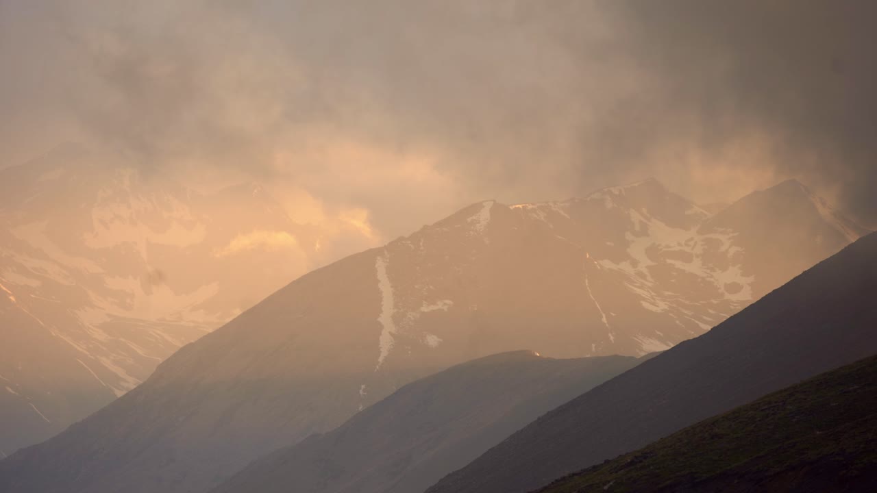 Stunning view of mountains with snow, clouds make view foggy, orange sunlight from sunset, sunrise, static, copy space