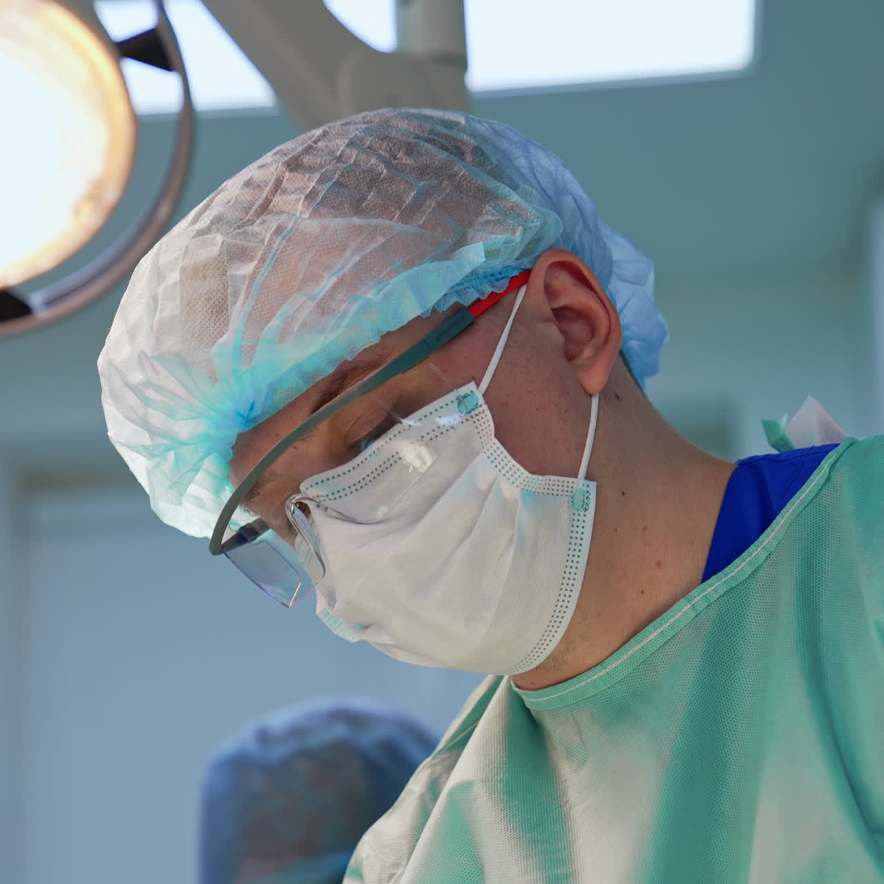Medico uomo con mascherina, cuffia e occhiali protettivi. Primo piano del ritratto di un chirurgo al lavoro.