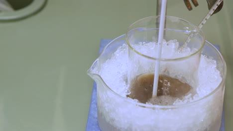 agitar la solución química en un vaso de precipitados mientras se enfría en hielo con un termómetro - tiro inclinado hacia abajo