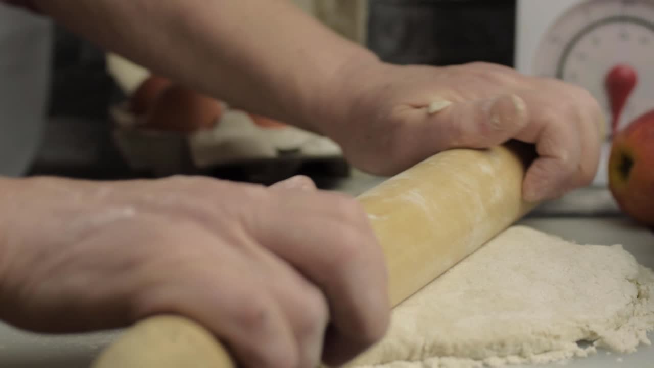 Hands using rolling pin in kitchen to roll dough medium shot