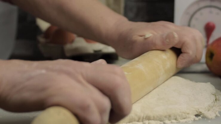 Hands using rolling pin in kitchen to roll dough medium shot