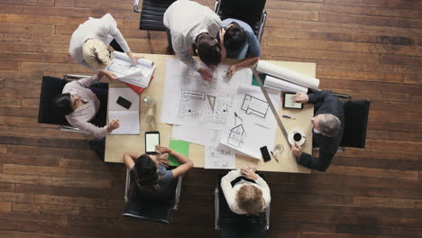 vista superior de personas de negocios que se reúnen alrededor de la mesa de la sala de juntas discutiendo planes arquitectónicos para un nuevo espacio de oficina compartido sostenible