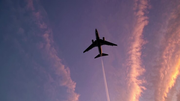 Dramatic low-angle shot of an airplane soaring against a vibrant sunset sky, capturing dynamic